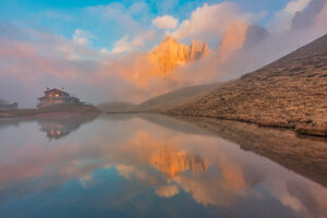 The iconic Baita Segantini reflected in the still waters at sunset with the Pale di San Martino peaks glowing in the evening light. Primiero San Martino di Castrozza, Trento province, Trentino, Italy The iconic Baita Segantini reflected in the still waters at sunset with the Pale di San Martino peaks glowing in the evening light. Primiero San Martino di Castrozza, Trento province, Trentino, Italy