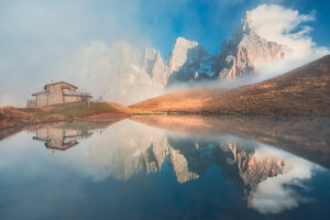 The iconic Baita Segantini reflected in the still waters at sunset with the Pale di San Martino peaks glowing in the evening light. Primiero San Martino di Castrozza, Trento province, Trentino, Italy The iconic Baita Segantini reflected in the still waters at sunset with the Pale di San Martino peaks glowing in the evening light. Primiero San Martino di Castrozza, Trento province, Trentino, Italy