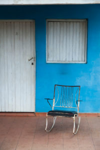 Caribbean, Cuba, Valle de Viñales, Viñales, rocking chair in front of blue house wall and white door Caribbean, Cuba, Valle de Viñales, Viñales, rocking chair in front of blue house wall and white door