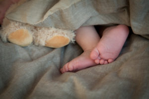 Newborn, baby, bare baby feet in bed next to teddy feet Newborn, baby, bare baby feet in bed next to teddy feet