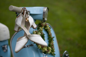 Rings and bridal shoes hang on the handlebar of a light blue Vespa Rings and bridal shoes hang on the handlebar of a light blue Vespa