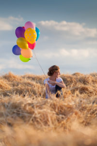 Young woman with colorful air balloons in a mowed grain field Young woman with colorful air balloons in a mowed grain field