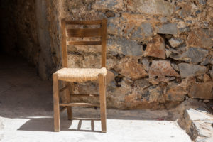brown wooden chair with braided seat, in front of stone wall, Spinalonga (former leprosy island) , Greece, Crete, Kalydon