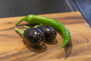 Harvesting aubergines and cooking them vegetarian: healthy and sustainable nutrition from your own garden. Two eggplants and a green pepper on a wooden board. Harvesting aubergines and cooking them vegetarian: healthy and sustainable nutrition from your own garden. Two eggplants and a green pepper on a wooden board.