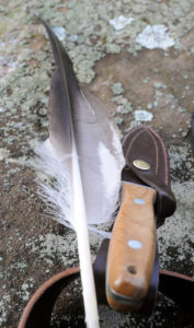 Eagle feather and falconer's knife on stone with patina, close-up Eagle feather and falconer's knife on stone with patina, close-up