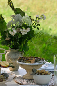 Vegane mangold quiche and white bunch of flowers on laid table, in the background blurred meadow, close up Vegane mangold quiche and white bunch of flowers on laid table, in the background blurred meadow, close up