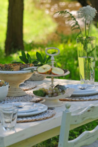 Mangold quiche and Etagere with sliced apple on white laid table, in the background blurred meadow and brook Mangold quiche and Etagere with sliced apple on white laid table, in the background blurred meadow and brook