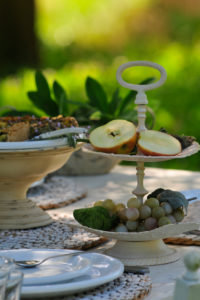 Etagere with sliced apple and grapes on white dining table, in the background blurred summer meadow Etagere with sliced apple and grapes on white dining table, in the background blurred summer meadow