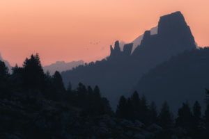 The striking rock formation Cinque Torri at sunrise in front of different layers of mountain ranges and hills in silhouette with a flock of birds The striking rock formation Cinque Torri at sunrise in front of different layers of mountain ranges and hills in silhouette with a flock of birds