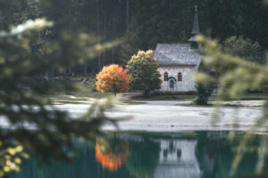 A church on Lake Braies / Pragser Wildsee which is reflected in this lake. Next to the church is a tree with the first red autumn leaves and it stands out. South Tyrol, Dolomites, Italy A church on Lake Braies / Pragser Wildsee which is reflected in this lake. Next to the church is a tree with the first red autumn leaves and it stands out. South Tyrol, Dolomites, Italy