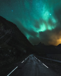 Nordlichter über den Fjorden der Insel Senja in Norwegen. Eine Straße führt ins Dunkle Nordlichter über den Fjorden der Insel Senja in Norwegen. Eine Straße führt ins Dunkle