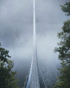 Die Hängeseilbrücke Geierlay am Morgen mit Nebel im Hunsrück. Eine Person befindet sich am Ende der Brücke Die Hängeseilbrücke Geierlay am Morgen mit Nebel im Hunsrück. Eine Person befindet sich am Ende der Brücke