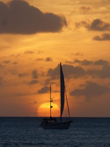 Sail boat in the distance at sea with setting sun Sail boat in the distance at sea with setting sun