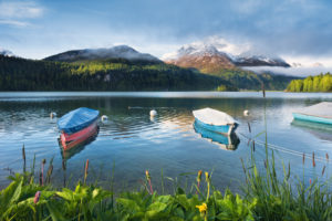 Idyllic scene on Lake Sils in the Engadin near St. Moritz, Swiss Alps, boats, blue water with reflection in the early morning light