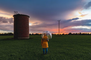 Sunset with rain. In the foreground a person with a raincoat and umbrella and a brick silo, in the background a spectacularly colored sky Sunset with rain. In the foreground a person with a raincoat and umbrella and a brick silo, in the background a spectacularly colored sky