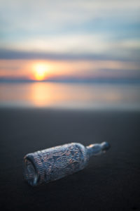 Glasflasche mit Verzierungen am Strand in abendlichem Licht Glasflasche mit Verzierungen am Strand in abendlichem Licht