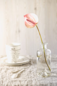 Still life with pink anthurium in a glass vase on table with bright linen cloth and tableware Still life with pink anthurium in a glass vase on table with bright linen cloth and tableware