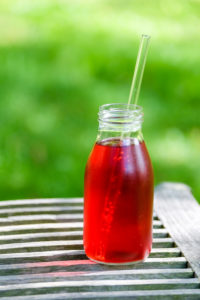 Small bottle with red lemonade on a wooden table in the garden Small bottle with red lemonade on a wooden table in the garden