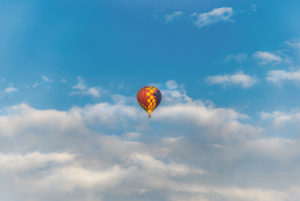Colorful, flying hot air balloon in front of cloudy summer sky Colorful, flying hot air balloon in front of cloudy summer sky