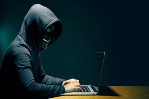 Side view of person wearing hooded top and Guy Fawkes face mask using laptop Side view of person wearing hooded top and Guy Fawkes face mask using laptop