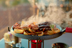Grilled mixed meats and vegetables sizzling on a hot serving platter with steam rising against a blurred background.