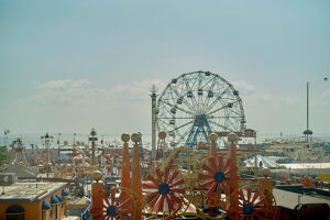 Sunny day at a bustling amusement park with Ferris wheel and colorful attractions.