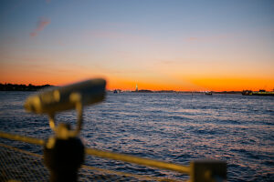 Sunset view over the water with a telescope in the foreground against a vibrant sky.
