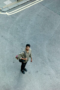 Aerial view of a man standing on a street corner with a bag, looking up. 