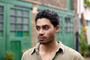 Young man with curly hair wearing a green shirt standing in front of a green door.