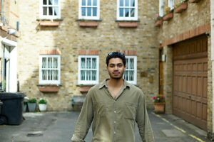 Young man standing in front of a brick house lined with windows and adorned with plants.