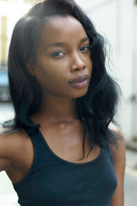 Young woman with long black hair wearing a black tank top, posing confidently on an urban street.