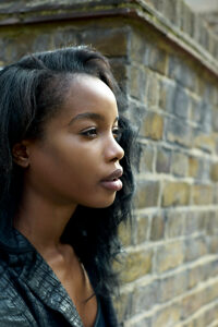 Side profile of a young woman with contemplative expression against a brick wall background.