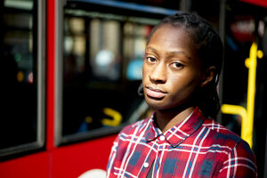 A thoughtful young man in a plaid shirt standing in front of a red bus.