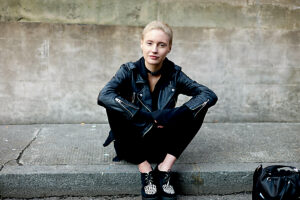 Young woman in a black leather jacket sitting on a curb.