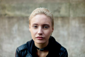 Portrait of a young woman with blonde hair and a leather jacket against a blurred background.