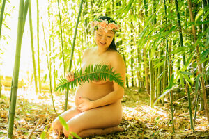 Pregnant woman sitting among bamboo, outdoors under sunlight. 