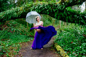 Pregnant woman in forest, holding umbrella, wearing a flowing purple skirt and flower headband. 