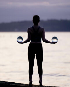 Silhouette of a woman holding crystal balls, standing by a serene lake at dusk. WA, USA