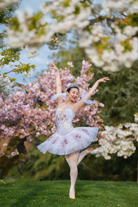 Ballerina in elegant tutu dances gracefully in a lush cherry blossom-filled garden. WA, USA