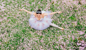 Ballet dancer in tutu poses gracefully on pink flower-covered field viewed from above. WA, USA