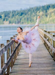 Ballerina performing an elegant arabesque on a wooden pier by a serene lake. WA, USA