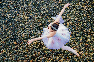 Ballerina in a white tutu gracefully poses on a pebble-covered beach. WA, USA
