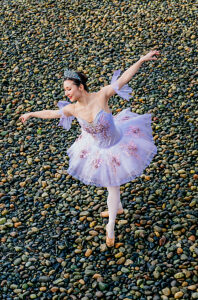 Ballerina in a lilac tutu dances gracefully on a pebbled surface. WA, USA