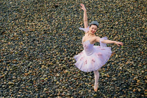 Ballerina in white tutu and tiara dances gracefully on a rocky beach. WA, USA