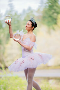 Ballerina in tutu holding crystal balls gracefully, with nature in the background. WA, USA