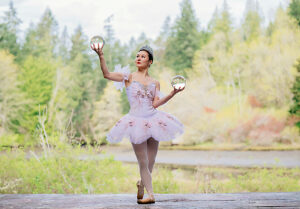 Ballerina in a lavender tutu balancing crystal balls amid a lush forest backdrop. WA, USA
