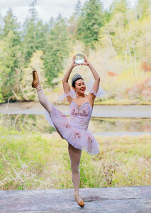 Ballerina in tutu striking elegant pose outdoors near a serene river and lush forest. WA, USA