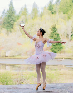 Ballerina in tutu striking elegant pose outdoors near a serene river and lush forest. WA, USA