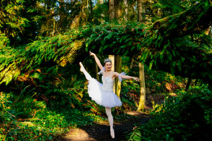 Ballerina in white dances gracefully on a forest path surrounded by lush green foliage. WA, USA