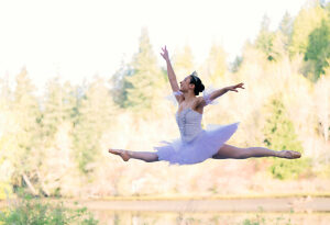 Ballerina leaps gracefully in a forest setting wearing a white tutu, exuding elegance and strength. WA, USA